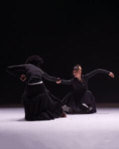 Contemporary dance duet using counterweight technique, two performers leaning away while connected by one hand on stage.