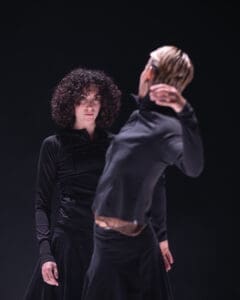 Two dancers face each other on stage in a tense and intimate contemporary duet.