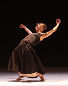 Contemporary dancer balances in an expressive pose under warm theatrical light during live performance.