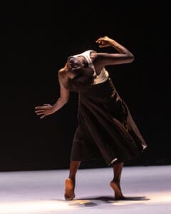 Solo dancer arches backward in an expressive contemporary pose under warm spotlight.