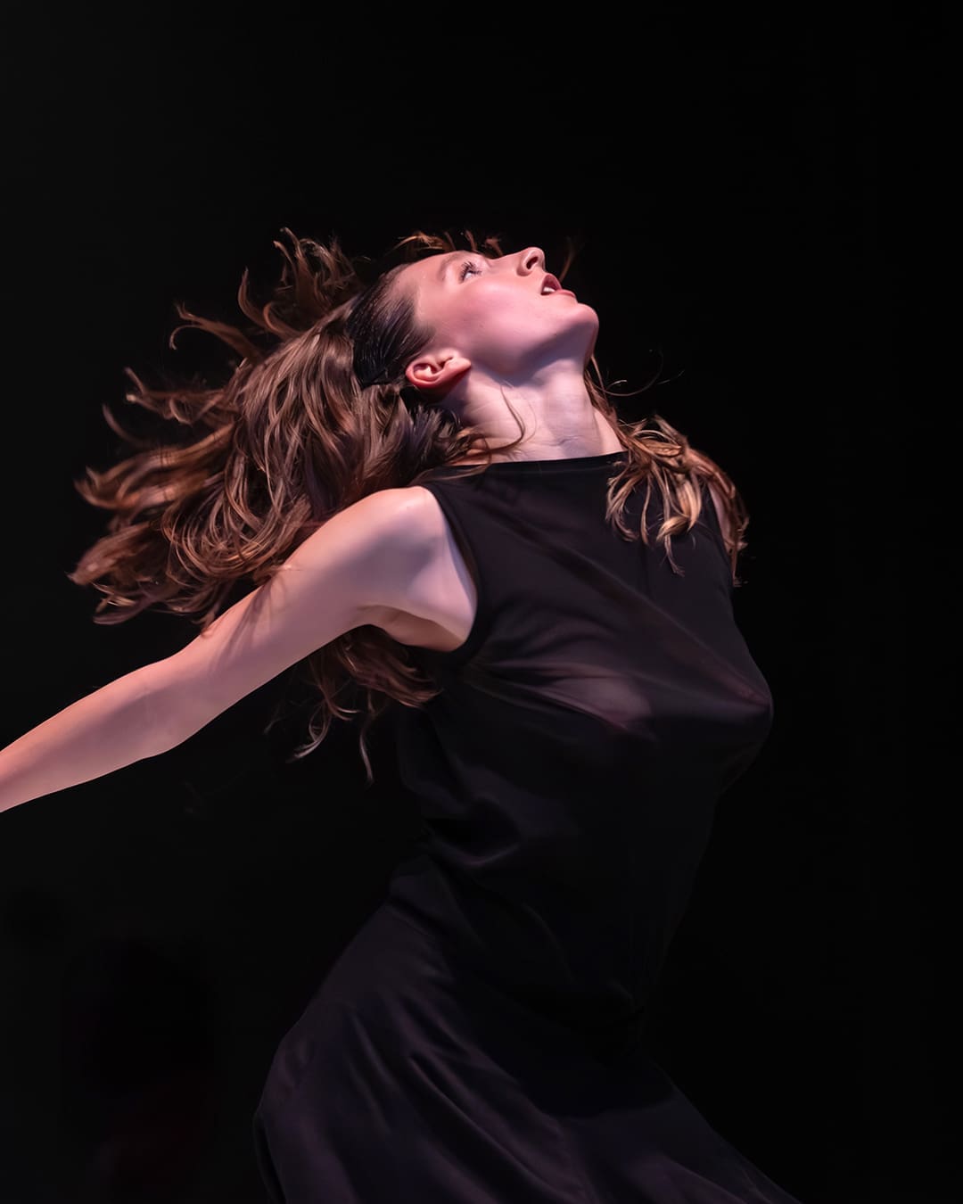 Female contemporary dancer throws her head back with flowing hair under dramatic stage lighting during Land of Hope by Cie Linga.